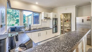 Una cocina moderna con armarios blancos, encimera de granito, horno empotrado y refrigerador de acero inoxidable.