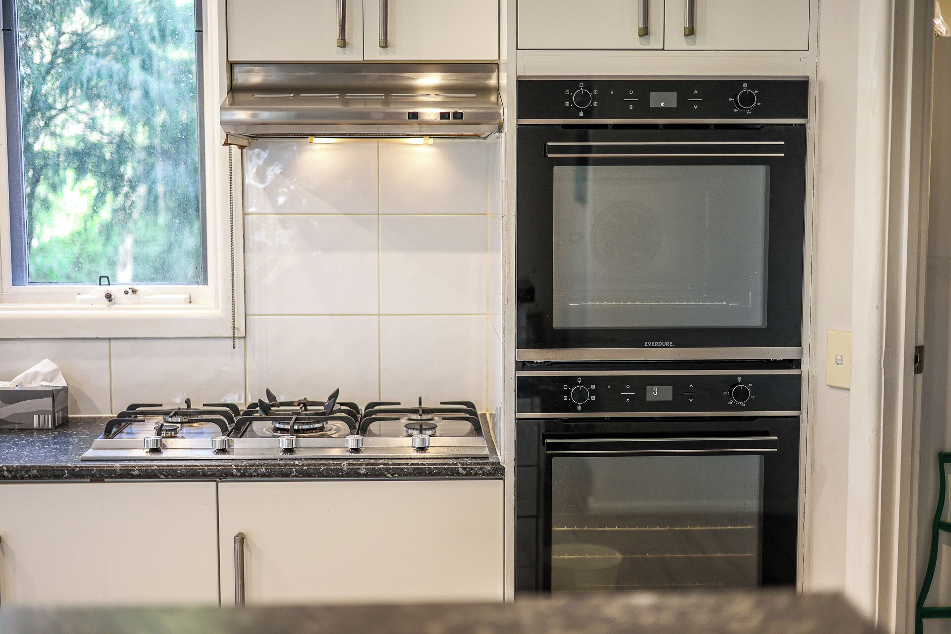 Une cuisine équipée de deux fours, d’une cuisinière à gaz et de meubles de rangement blancs.