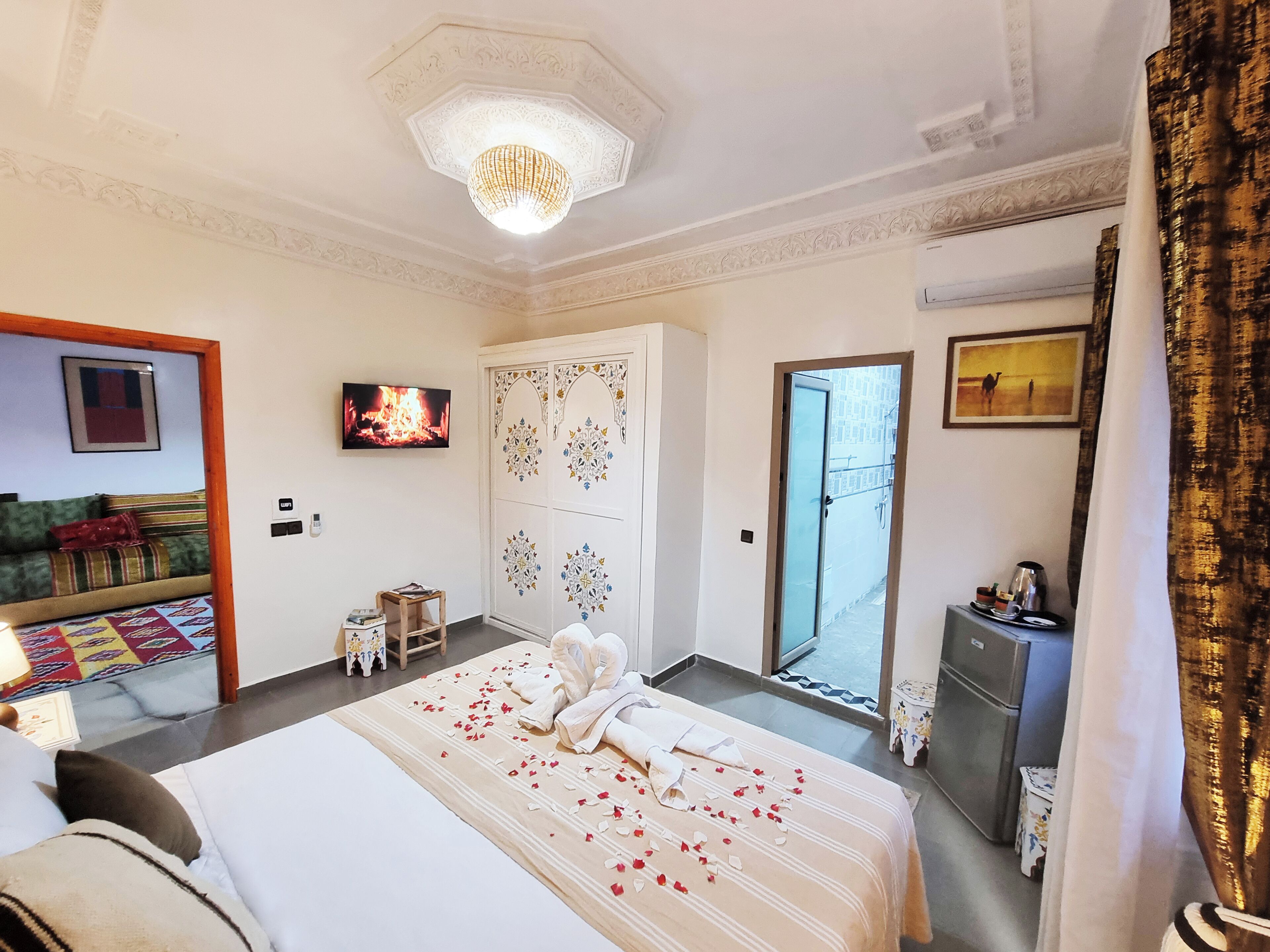 A hotel room with a bed, a television, a sofa, a decorative ceiling, and a door leading outside.