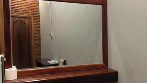Une salle de bain avec un miroir encadré en bois, des toilettes et une poubelle.