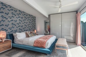 A modern bedroom with a large bed, a bedside table with a lamp, a bench, a wardrobe, and a large window with curtains.