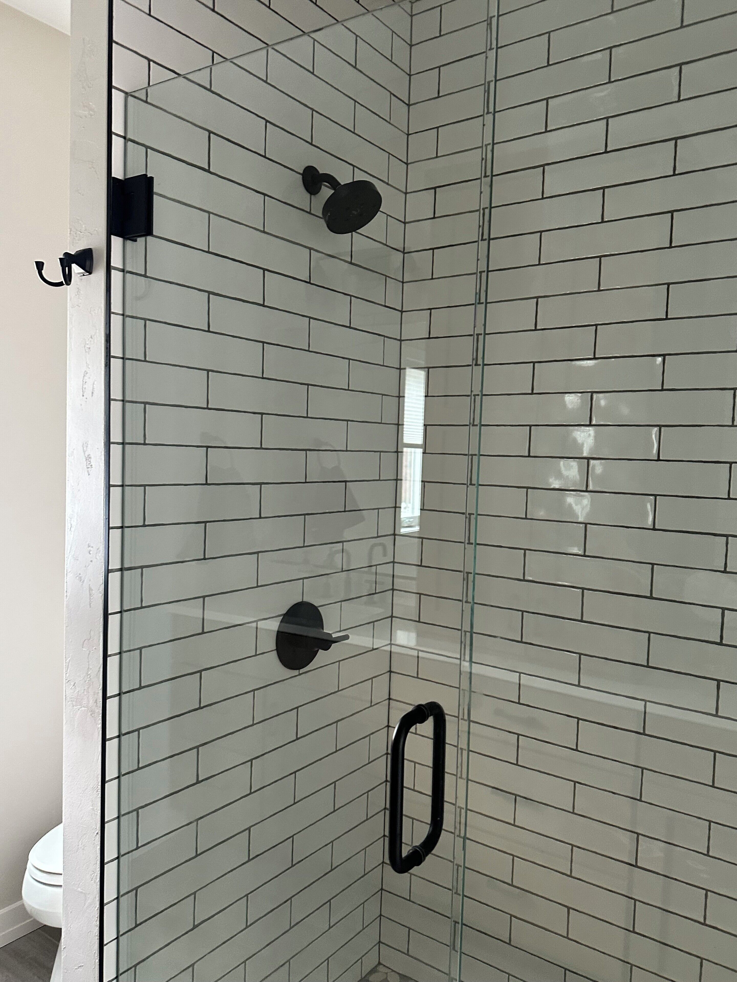 Un baño con paredes de azulejos tipo metro blancos, cerramiento de ducha de vidrio y un inodoro blanco.