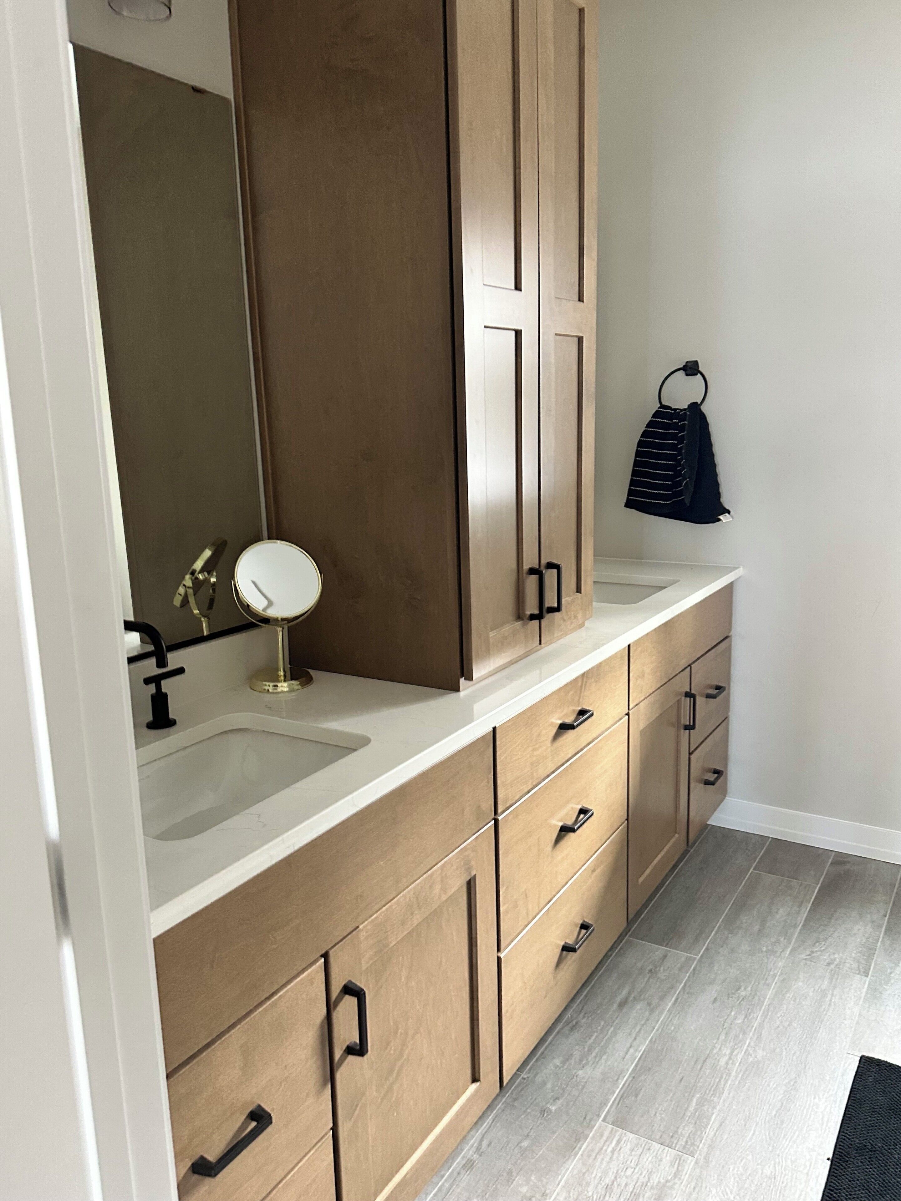 A bathroom with a large mirror, wooden cabinets, and a white countertop.