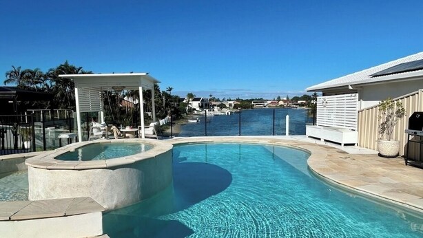 Ein Pool mit geschwungenem Design, einer überdachten Sitzgelegenheit und Blick auf das Wasser.