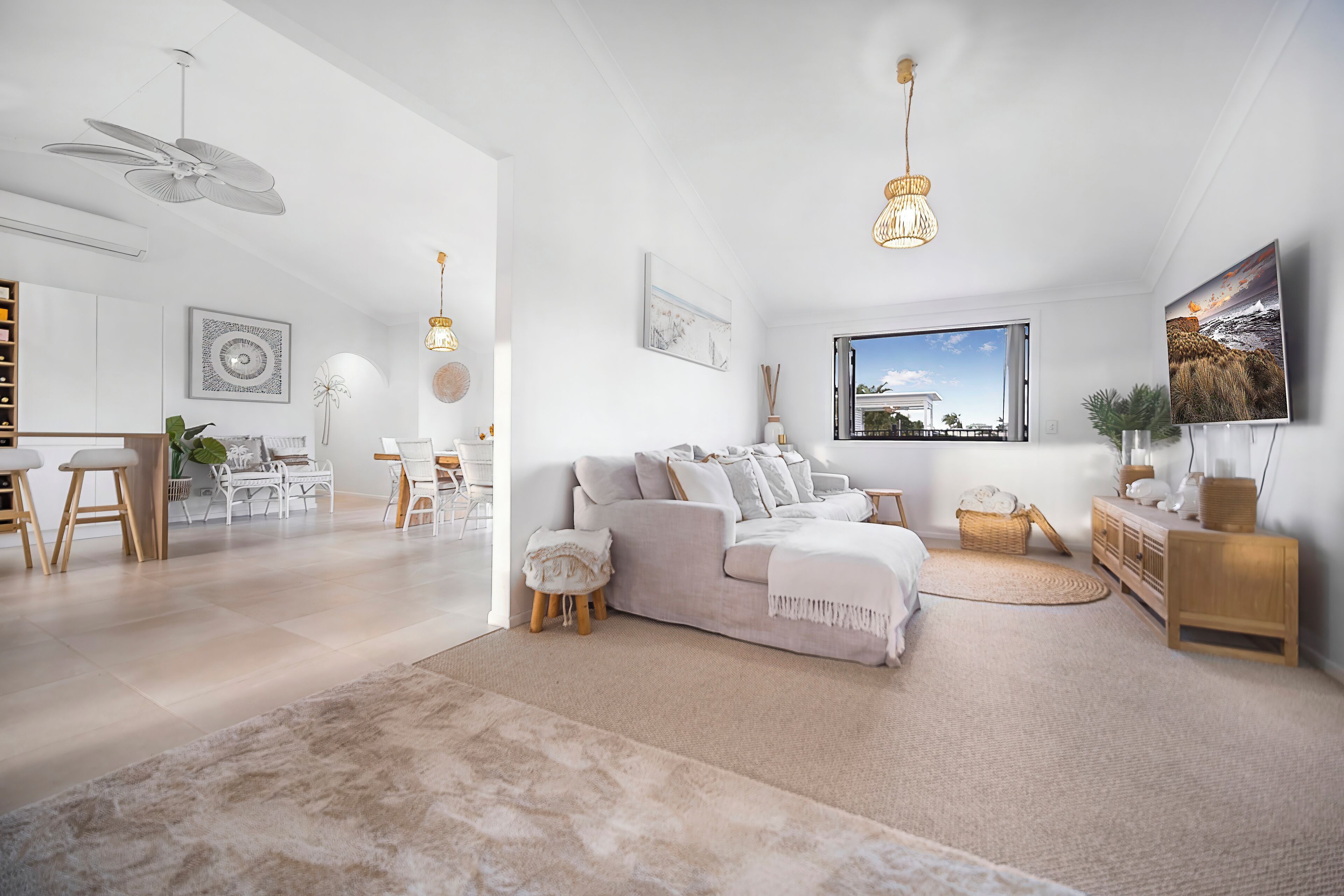 A modern living room with a white sofa, a dining area with a white table, and a large window with a view of the sea.