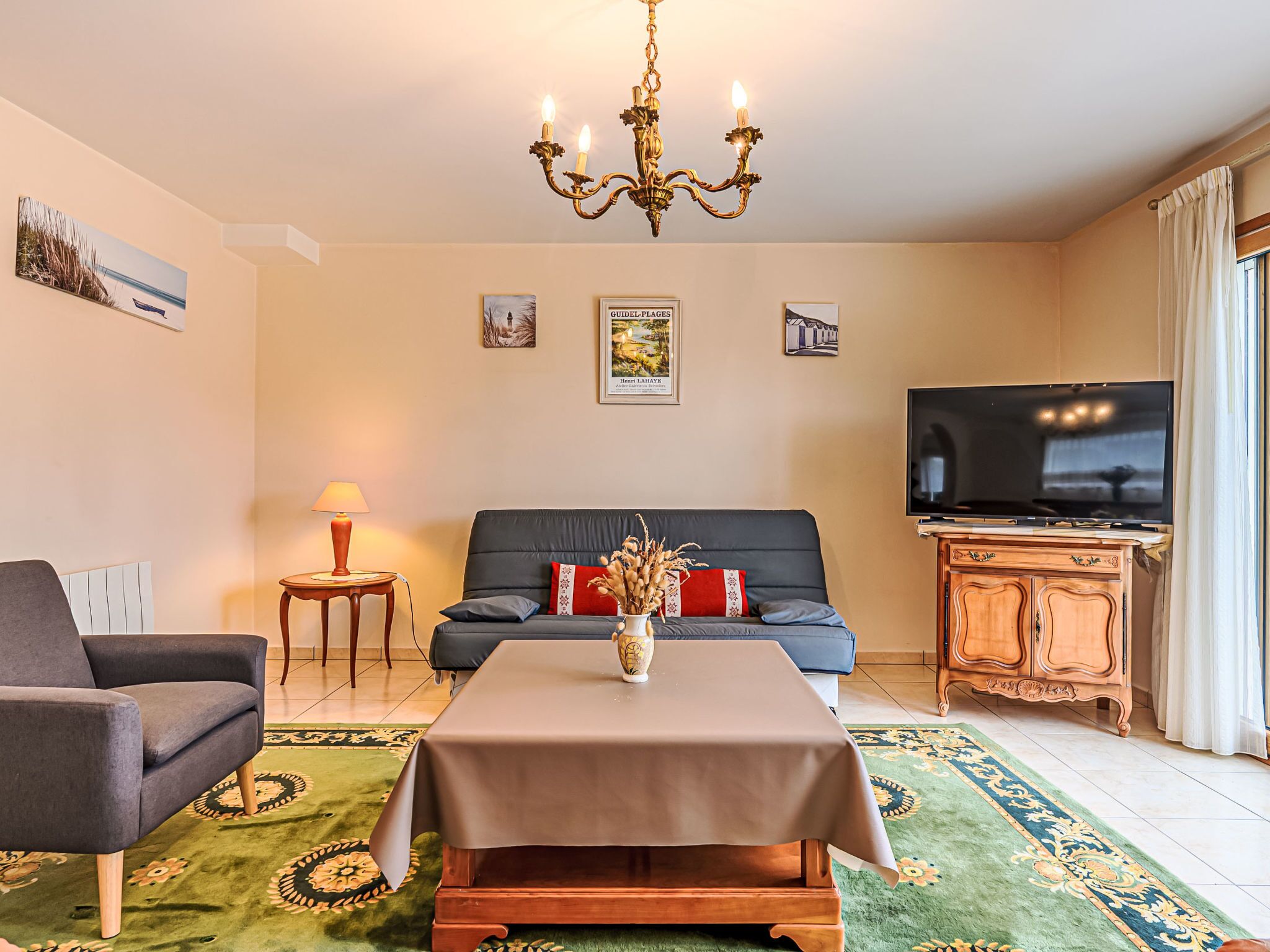 A living room with a sofa, a television, a chandelier, and a table with a vase.
