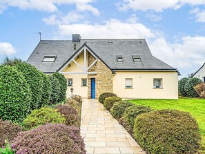 A two-story house with a stone facade, a blue door, and a paved driveway leading to the entrance.