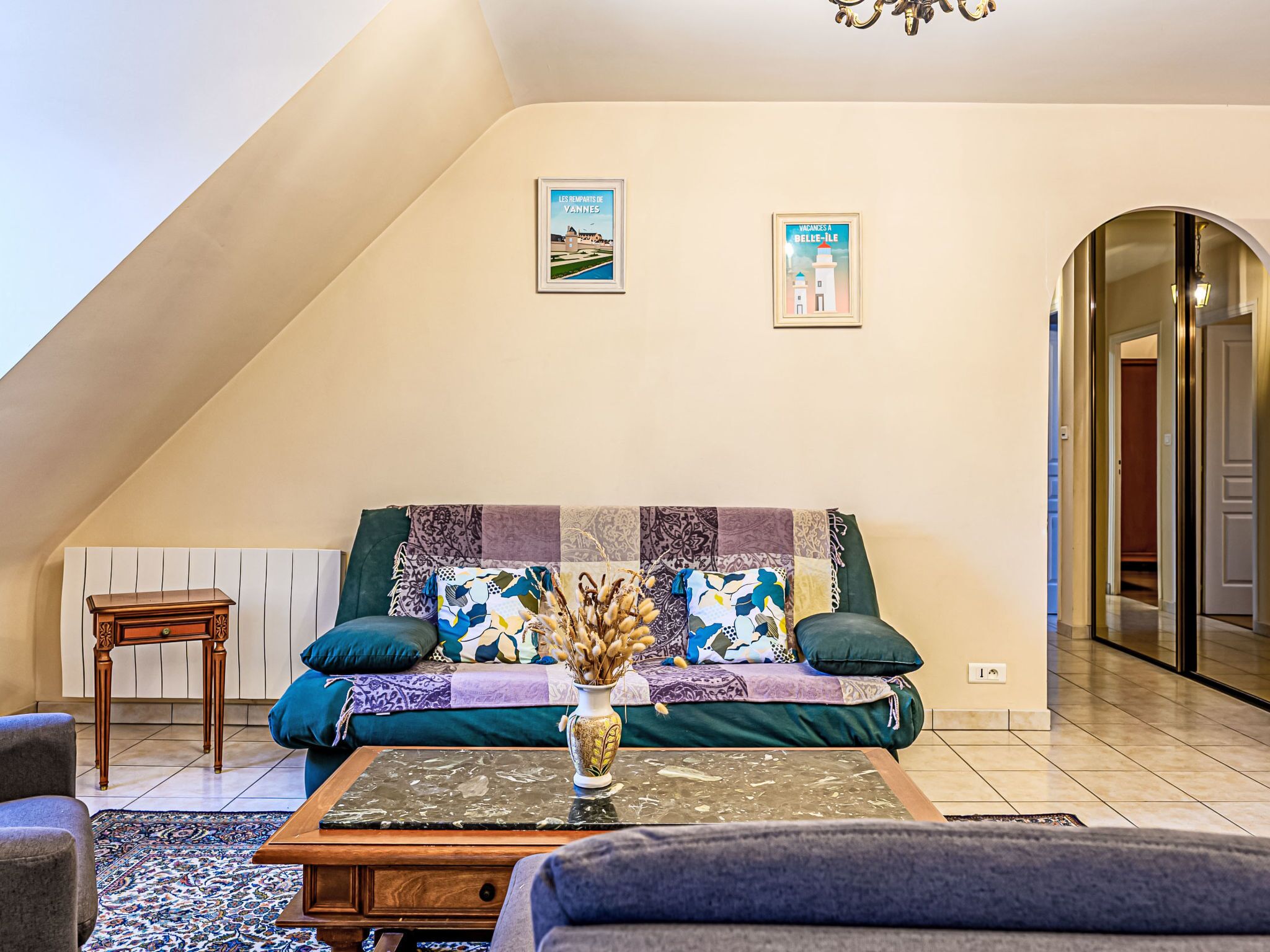 Un salon chaleureux avec un plafond haut, un canapé agrémenté de coussins à motifs, une table basse en bois et deux tableaux encadrés accrochés au mur.
