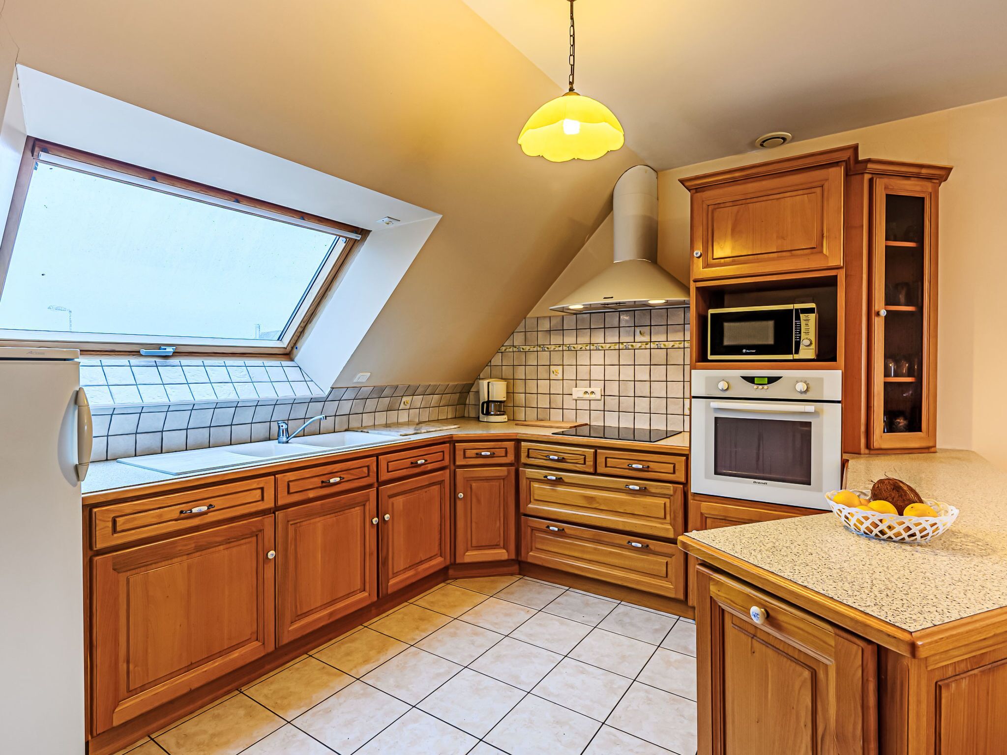 Una cocina con armarios de madera, microondas integrado, horno, ventana y tragaluz.