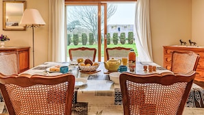 A dining area with a table set for four, surrounded by wicker chairs, a lamp, and a view of a garden through large windows. - Le Prat by Interhome (Guidel)