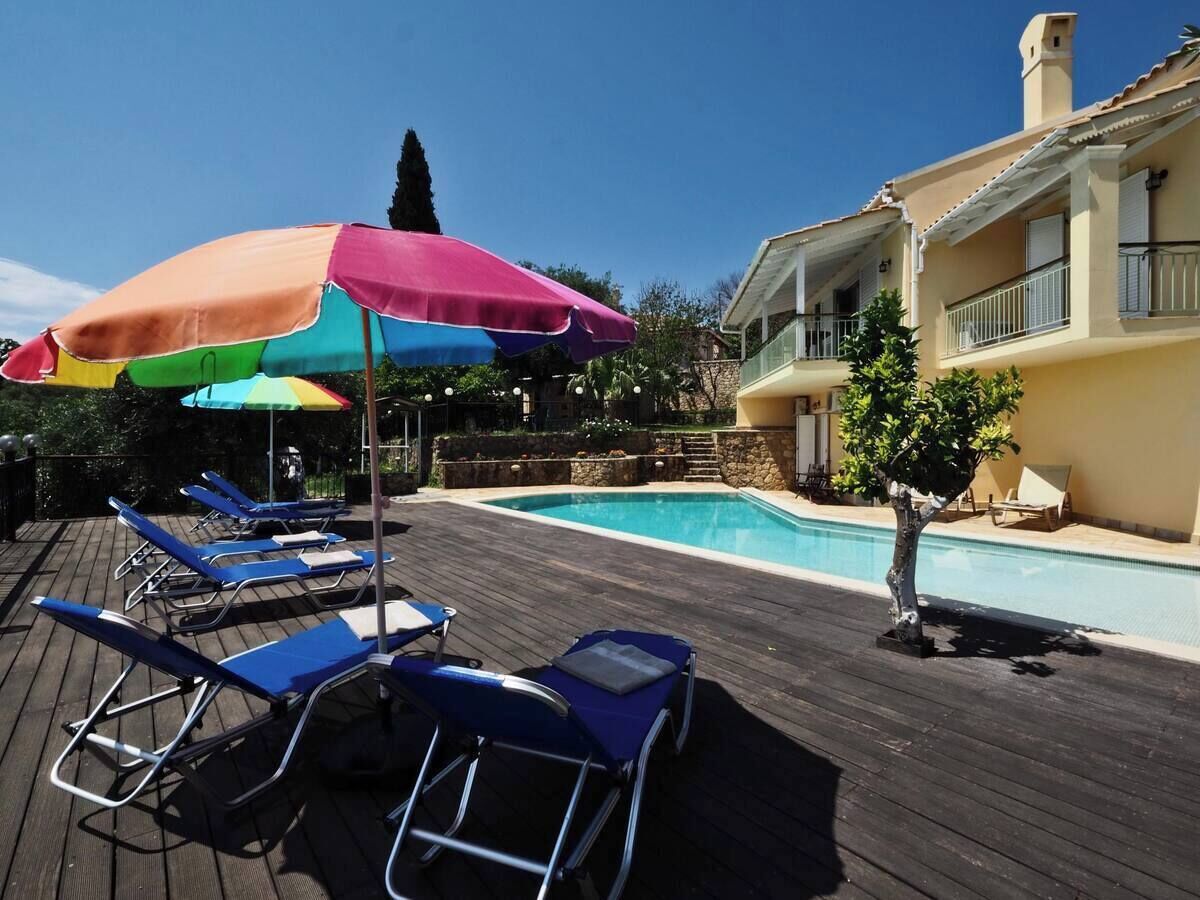 Ein Poolbereich mit Liegestühlen und Sonnenschirmen, ein Schwimmbecken und ein Gebäude mit Balkonen.