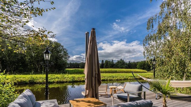 A deck with outdoor seating, a lamp, and a view of a water body and greenery. - 6 pers. Veenhuis Comfort Plus by Interhome (Vlagtwedde)