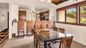 Un comedor con una mesa de vidrio y sillas de madera, una cocina al fondo y vistas al exterior a través de amplios ventanales.