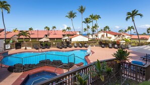 Zona de piscina en un resort con numerosas tumbonas y sombrillas, rodeada de palmeras y edificios con techos rojos.