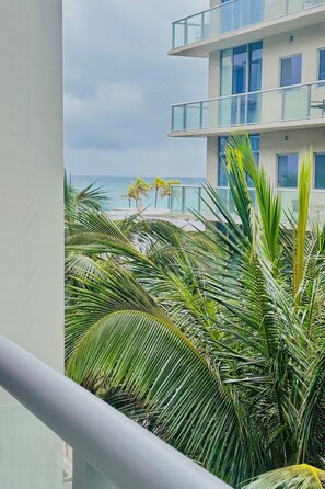 Un balcon donnant sur une plage, des palmiers et un immeuble moderne doté de balcons.