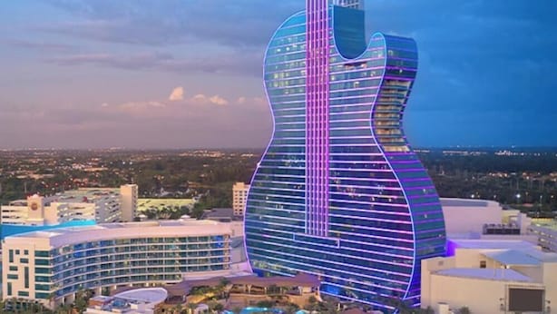 Un edificio grande con forma de guitarra, rodeado de otros edificios y un paisaje urbano.