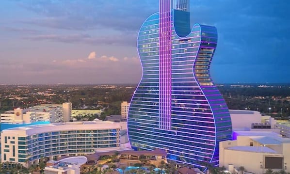 A large building with a guitar shape, surrounded by other buildings and a cityscape.