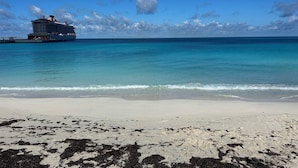 Ein Strand mit klarem, türkisblauem Wasser und einem vor dem Steg liegenden Kreuzfahrtschiff.