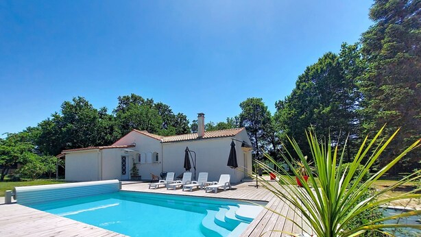 Une piscine avec des chaises longues, une terrasse en bois et un bâtiment blanc avec un toit rouge.