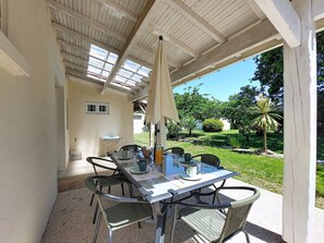 Een terras buiten met een tafel en stoelen, een pergola erboven en uitzicht op een tuin.