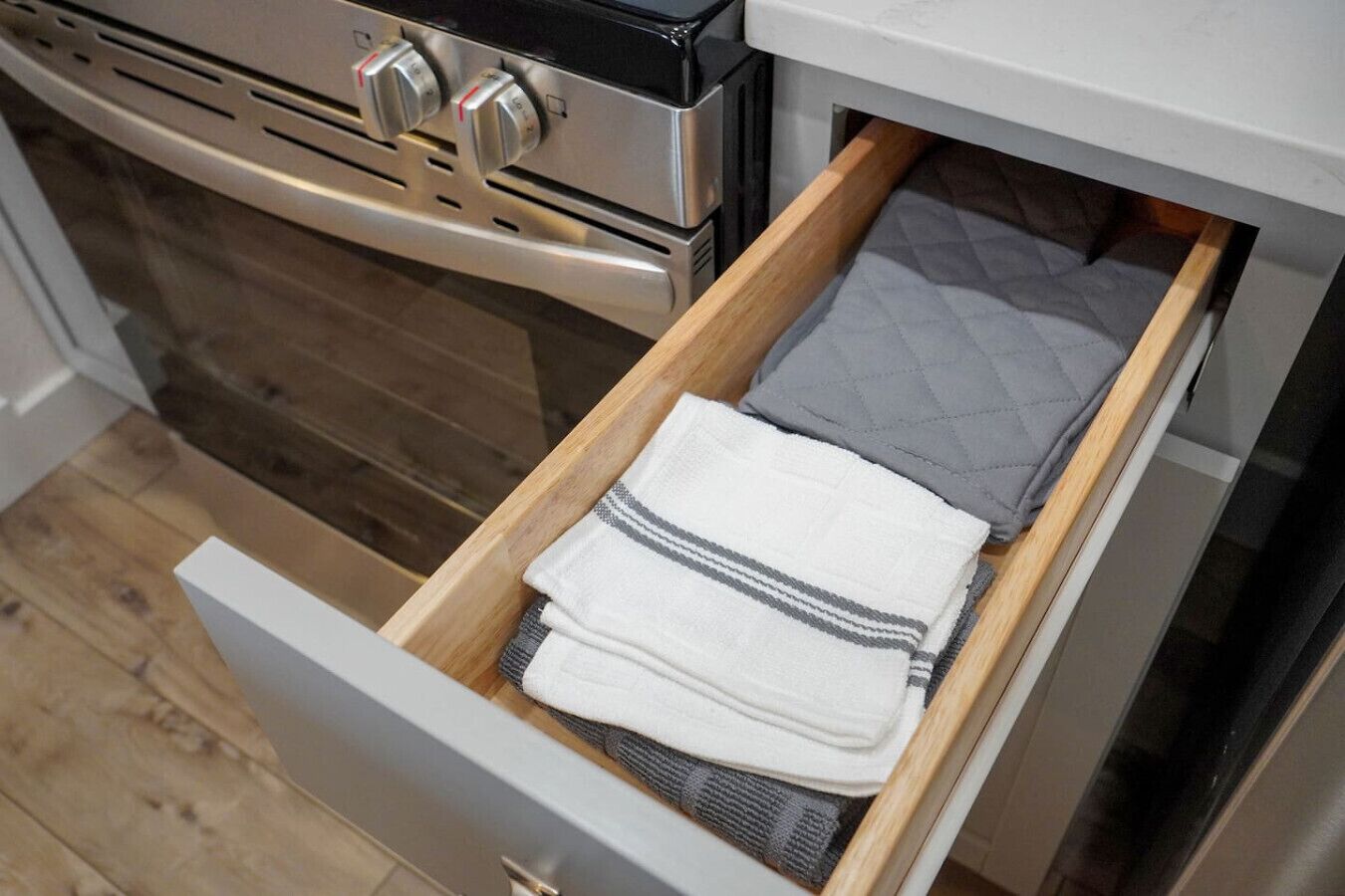 A kitchen with a stainless steel oven and a wooden drawer containing folded towels.