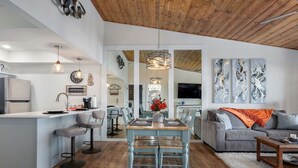 A modern kitchen with a bar area, a dining table with chairs, a grey sofa, and abstract wall art. - Lakeview Getaway at Kimberling Crossing (Kimberling City)