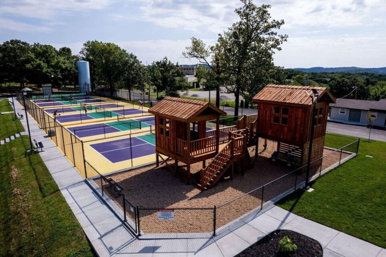 Un parque infantil con una cancha de baloncesto, dos casitas de madera y una zona vallada.