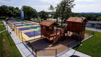 Un parque infantil con una cancha de baloncesto, dos casitas de madera y una zona vallada.