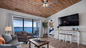 A modern living room with a wooden ceiling, a large TV, a balcony with a view, and a cozy seating area. - Lakeview Getaway at Kimberling Crossing (Kimberling City)