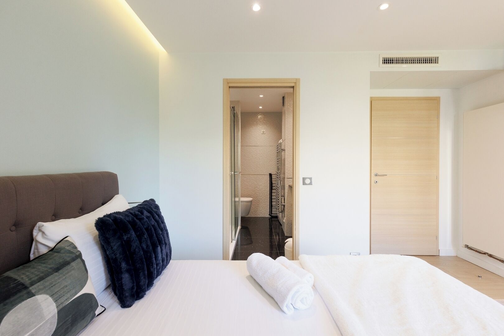Une chambre d’hôtel moderne, dotée d’un grand lit, d’un canapé et d’une salle de bain visible à travers une porte ouverte.