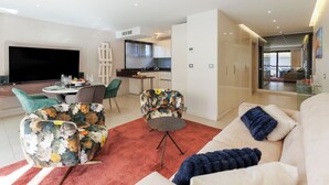 Una sala moderna con sofá, sillas, televisor y zona de comedor con mesa y sillas.