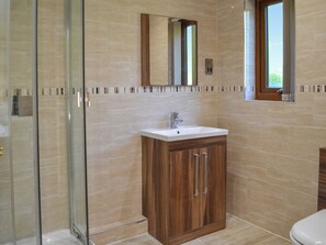 Ein Badezimmer mit Duschkabine aus Glas, einem Holzkosmetikschrank mit Waschbecken und einem Fenster über der Toilette.