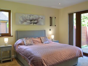 Une chambre à coucher avec un grand lit, deux tables de chevet, une commode, un miroir fixé au mur et une fenêtre avec des stores.