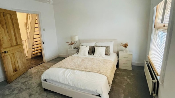 A bedroom with a bed, bedside tables, a chandelier, and a window with blinds. - House - Sleeps 5- Garden - Parking (Windsor)