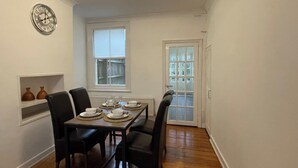 A dining area with a table set for four, chairs, a clock on the wall, and a window with a view of a wooden deck. - House - Sleeps 5- Garden - Parking (Windsor)