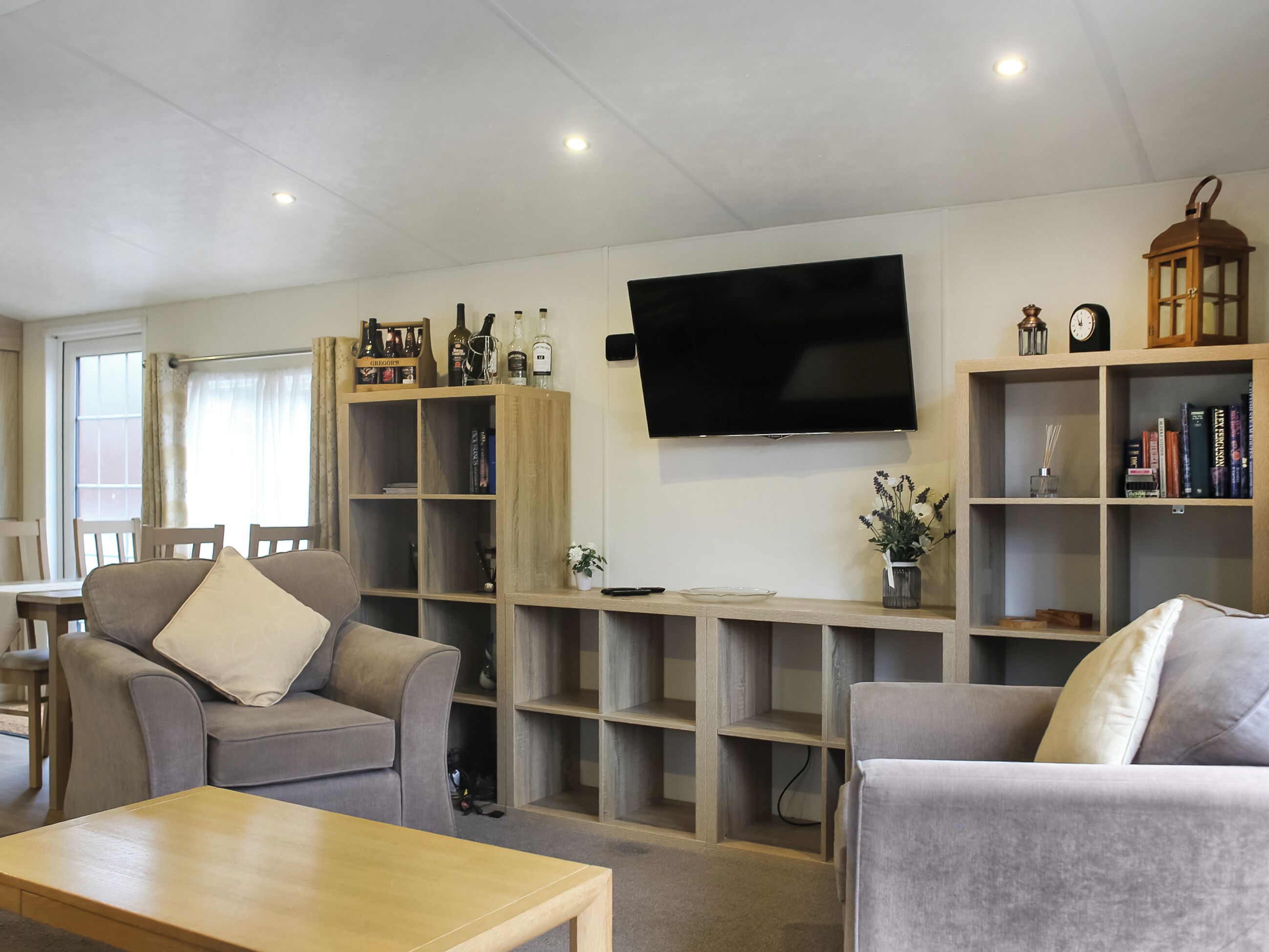 Una sala de estar con dos sofás, una mesa de centro, un televisor y estanterías empotradas con libros y objetos decorativos.