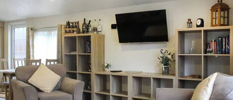 Una sala de estar con dos sofás, una mesa de centro, un televisor y estanterías empotradas con libros y objetos decorativos.