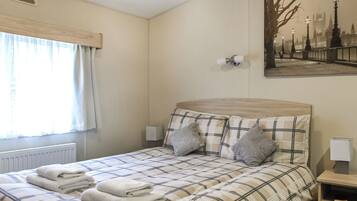 A bedroom with a bed, pillows, a bedside table, a lamp, a radiator, a window with curtains, and a painting on the wall.
