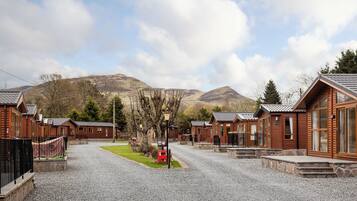 A row of wooden cabins with a gravel driveway, a red mailbox, and a mountain in the background.