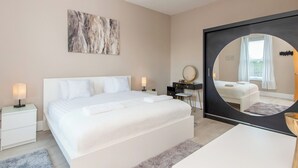 Une chambre moderne avec un grand lit, des tables de chevet, un miroir et une œuvre d’art murale.