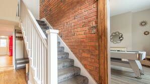 Un escalier dont les marches sont recouvertes de moquette et qui possède des rampes blanches, menant à une pièce avec un mur en briques et un miroir accroché au mur.