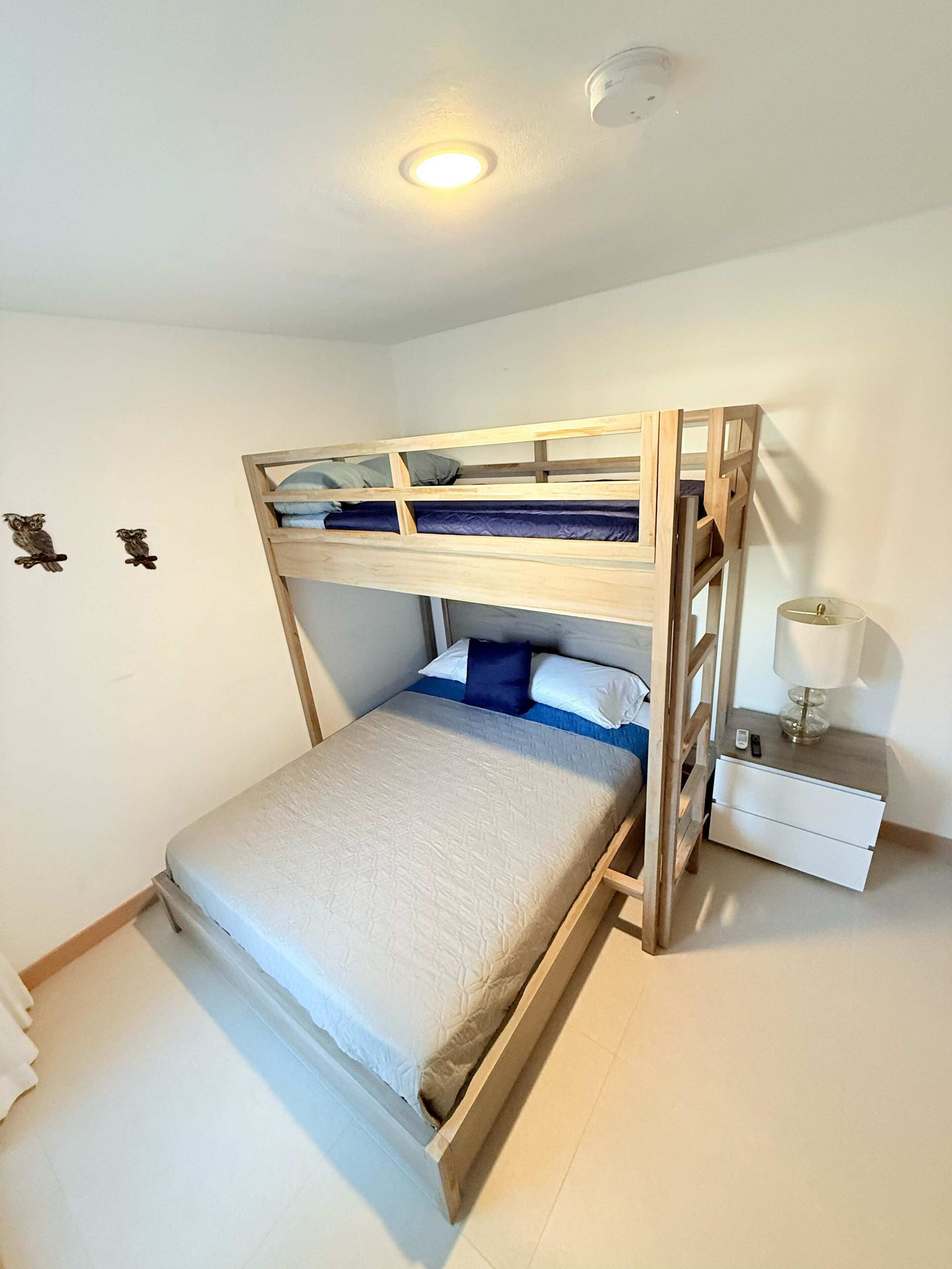 A bunk bed with a wooden frame, a bedside table with a lamp, and two owl wall decorations.