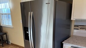 Ein Edelstahl-Kühlschrank von Whirlpool in einer Küche mit Holzboden und weißen Schränken.