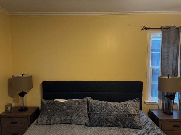Un dormitorio con cama, dos mesitas de noche y una ventana con cortinas.