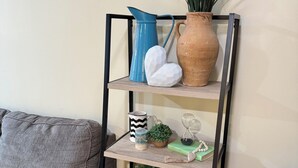 Ein Holzregal mit Dekorationselementen, darunter eine Vase, eine blaue Kanne und ein Blumentopf.