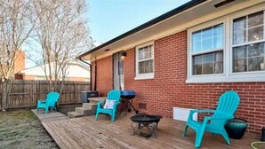 Eine überdachte Terrasse mit Holzdeck, zwei türkisfarbenen Adirondack-Stühlen, einem kleinen runden Tisch und einem Grill.