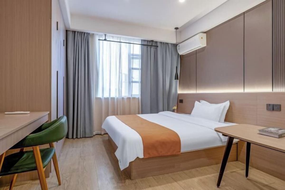 A hotel room with a bed, desk, chair, and an air conditioning unit.