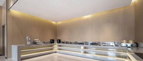 A modern hotel lobby with a long reception desk, a coffee machine, and a water dispenser.