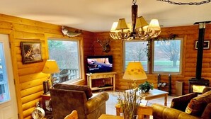 Interior acogedor de una cabaña de troncos con una mesa de comedor de madera, sofás de cuero, un televisor y una chimenea.