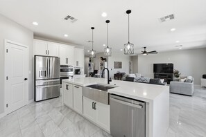A modern kitchen with stainless steel appliances, a central island with a sink, and pendant lighting. - SunHaven Retreat • Poolside Fun in Tempe w/ Spa, Game Room & RV Parking (Tempe)